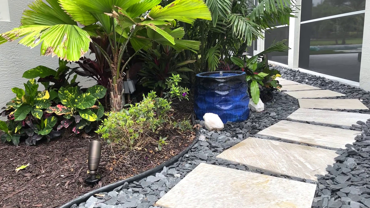 Rumba Fountain in Riviera Blue surrounded by tropical landscaping beside a decorative stone pathway