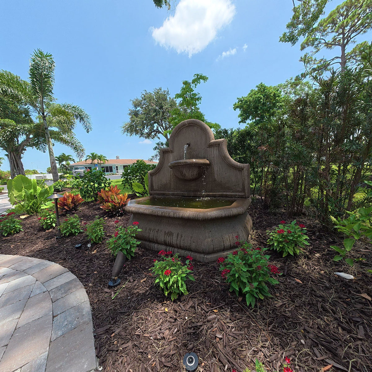 Andalusia cast stone fountain installed among colorful flowers and tropical landscaping