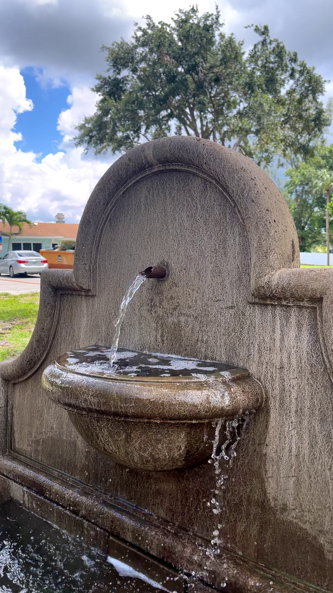 Angled view of the Andalusia Fountain featuring a cast stone wall design with a copper spout flowing into a rounded basin