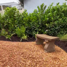 Arles cast stone garden bench surrounded by lush tropical landscaping in a backyard garden