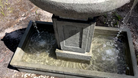 Close-up of the Austin Fountain's square catch basin with cascading water and geometric cast stone pedestal