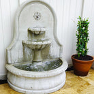Close view of the Estancia cast stone fountain showing cascading water, tiered bowls, and decorative back panel