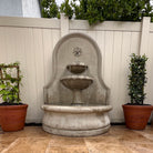 Estancia cast stone wall fountain with cascading water and tiered bowls in an outdoor patio setting