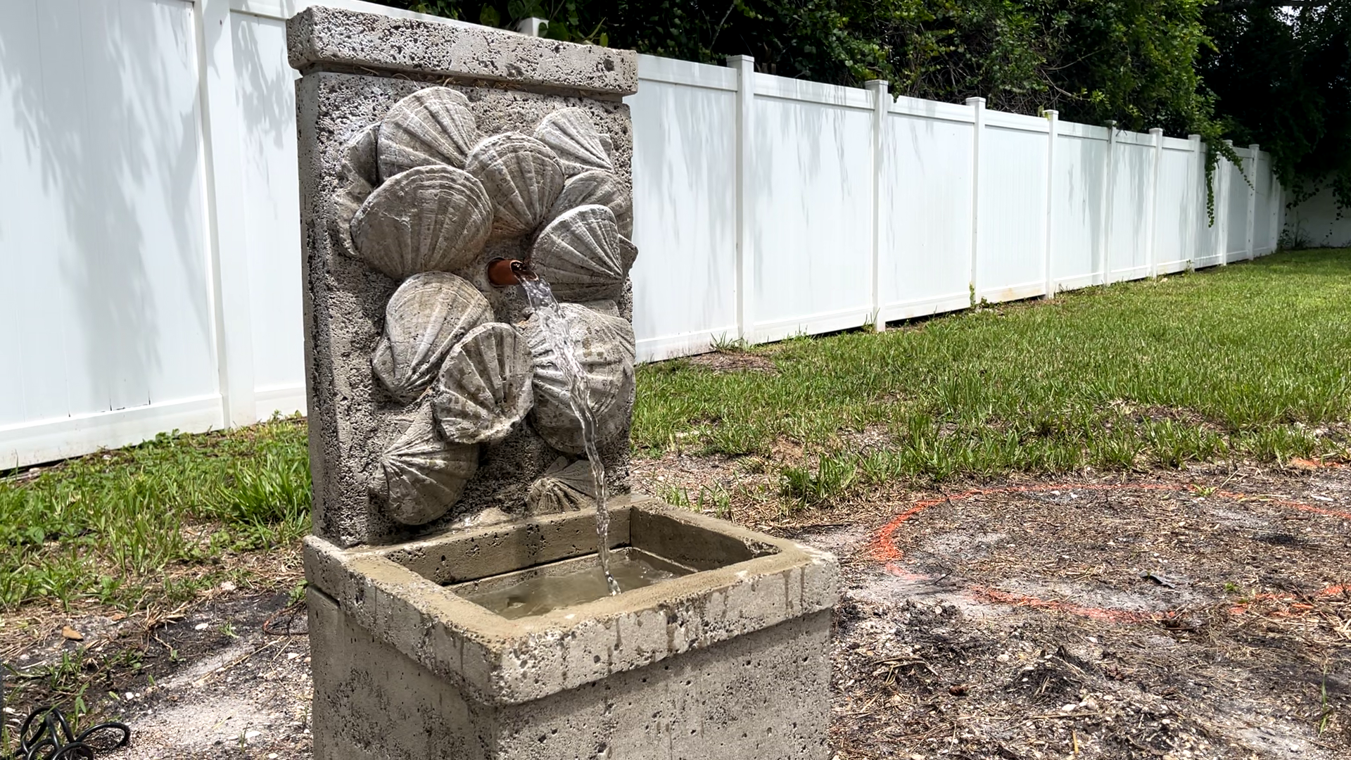 Angled view of the Nassau Wall Fountain showcasing the handcrafted cast stone seashell design and cascading water