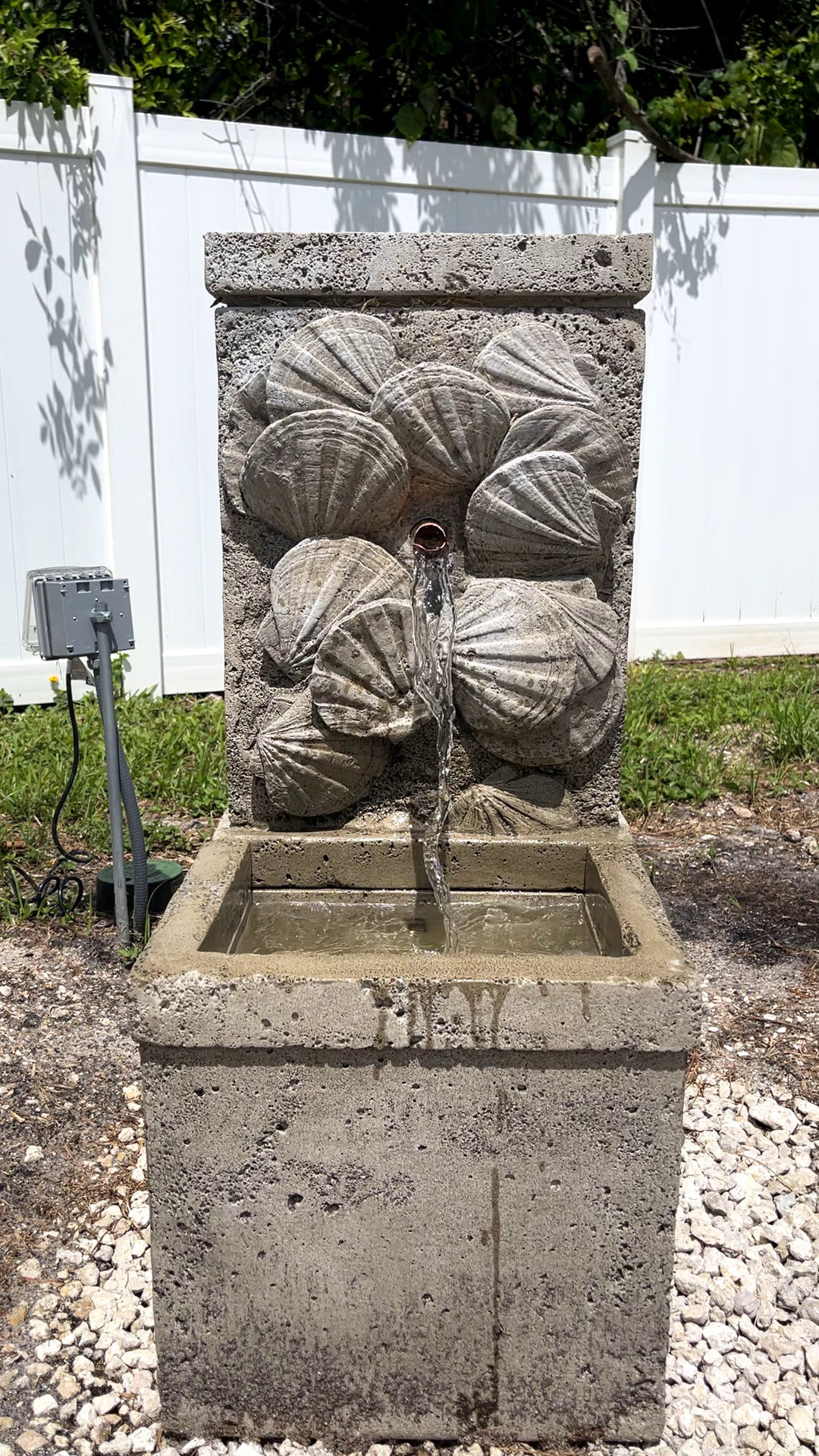 Nassau Wall Fountain with decorative seashell relief and flowing water viewed from the front in a landscaped outdoor setting