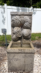 Nassau Wall Fountain with decorative seashell relief and flowing water viewed from the front in a landscaped outdoor setting