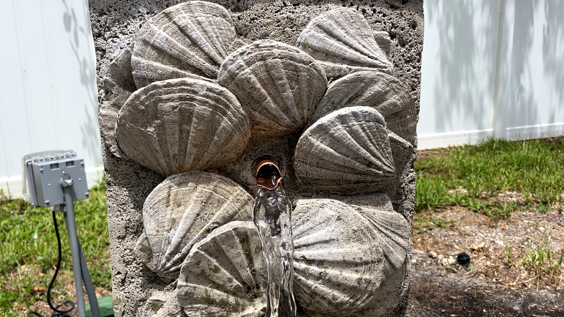 Close-up of the Nassau Wall Fountain highlighting the copper water spout, flowing water, and detailed cast stone seashell relief