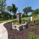 Provence cast stone fountain with four-sided column and flowing water installed in a landscaped garden
