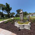 Angled view of the Provence cast stone fountain with central column and flowing water in an outdoor garden setting