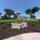 Provence Fountain surrounded by flowering landscape beds with water flowing into its quatrefoil cast stone basin